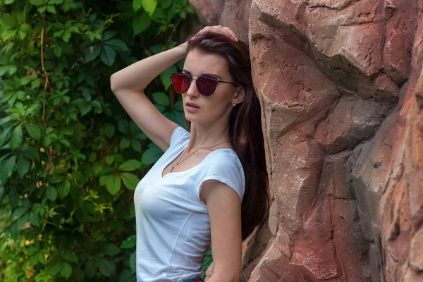 Retrato de una hermosa dama en gafas de sol que posa cerca de una pared de piedra — Foto de Stock