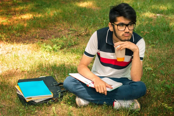 Smutne, młody student siedzi na trawie z kawy w rękach i książek na bok — Zdjęcie stockowe
