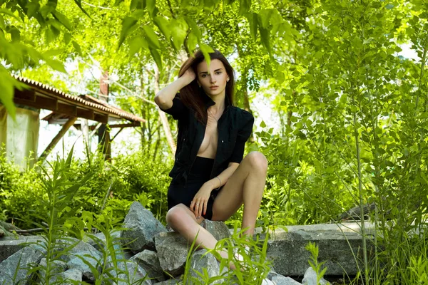 Beautiful sensual girl in black suit seated on rocks — Stock Photo, Image