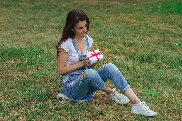 Mignonne brune s'assoit sur l'herbe et tient un petit emballage cadeau — Photo