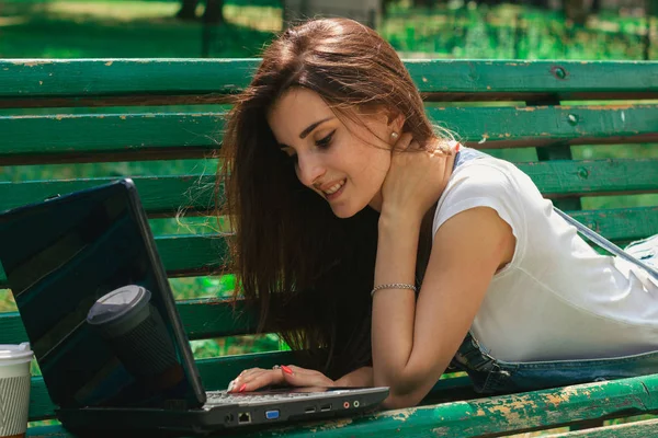 Портрет улыбающихся красивых брюнеток с ноутбуком на скамейке — стоковое фото