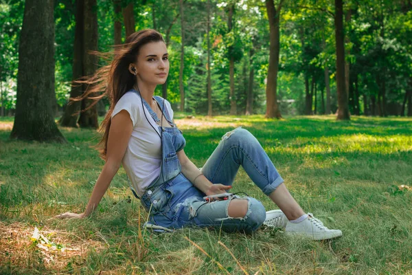 Lovely girl sits on green grass and her hair fly away in the wind — Stock Photo, Image