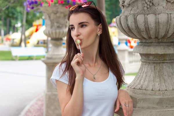 Beautiful young woman looks away and licks a lollipop — Stock Photo, Image