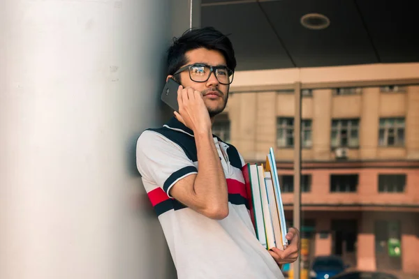 Charmig kille i glasögon på telefonen och håller en bok — Stockfoto