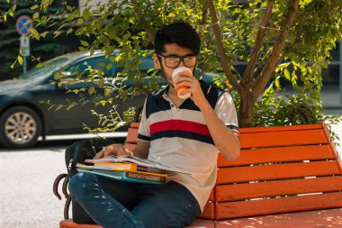 kahve içme ve bir kitap bir bankta oturan çekici öğrenci