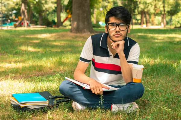 Młody facet stylowe okulary, siedząc na trawie z książek — Zdjęcie stockowe
