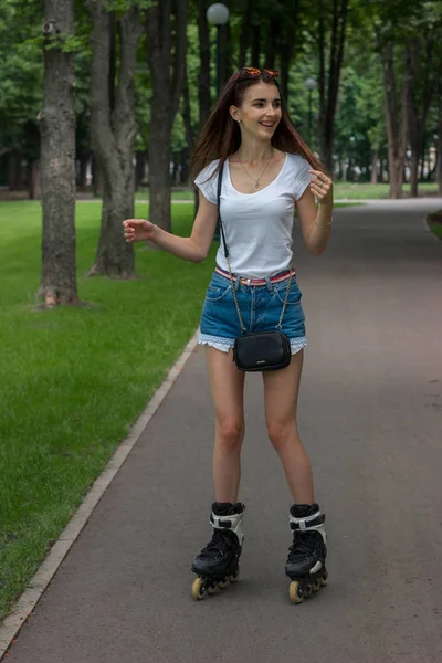 Glad ung tjej skrattar och skridskor på rullskidor på park — Stockfoto