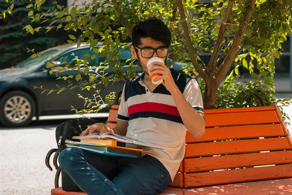Glamoureuze student zittend op een bankje koffie drinken en een boek houden — Stockfoto