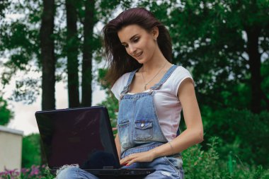 Sevimli genç kız parkta bir dizüstü bilgisayar kullanarak