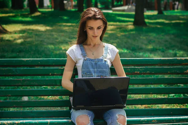 Joven hermosa chica en un banco usando un ordenador portátil — Foto de Stock