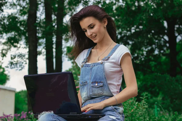 Sevimli genç kız parkta bir dizüstü bilgisayar kullanarak