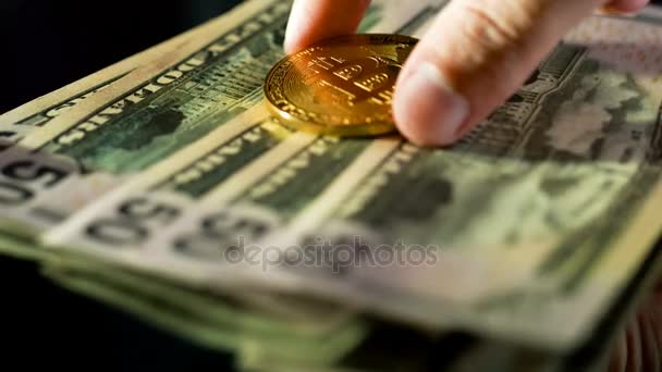 Close up van man zet een gouden bitcoin over een dollar biljetten — Stockvideo
