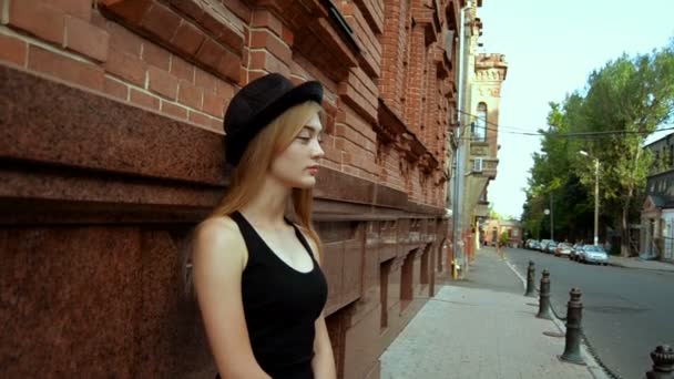 Beautiful young blonde in a black hat stands on a street — Stock Video