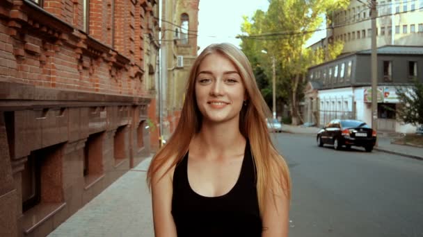 Prachtige blonde stands op straat kijkt naar de camera en glimlach — Stockvideo