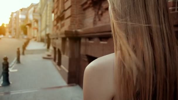 Молодая девушка со светлыми волосами идет по улице — стоковое видео
