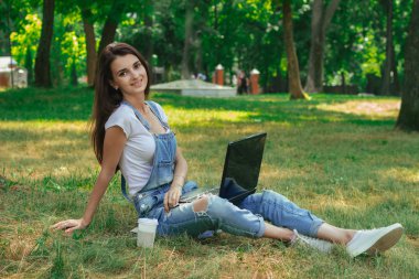 bir dizüstü bilgisayar ile parkta çimlerde oturan güzel hanımefendi