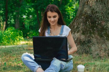 parkta büyük siyah dizüstü bilgisayar ile oturan genç gülümseyen Bayan