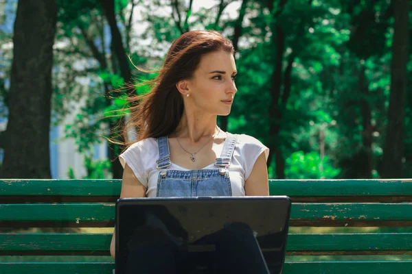 siyah bir dizüstü bilgisayar ile bir bankta genç esmer