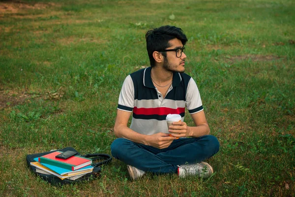 緑の芝生に若い魅力的な男座って一杯のコーヒーを保持しています。 — ストック写真