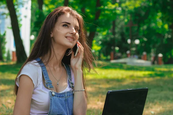 güzel kız yaz parkta bir dizüstü bilgisayar ile telefonda diyor