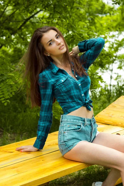 Mince belle fille en chemise à carreaux est assis sur un banc — Photo