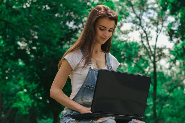 Güzel bir kızın ağaçları bir dizüstü bilgisayar ile zemin karşı parkta portre
