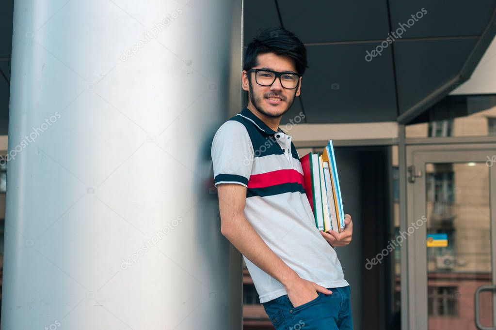smiling nice guy stands near the columns keeps books