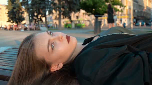 La belle jeune femme est allongée sur un banc dans la rue — Video