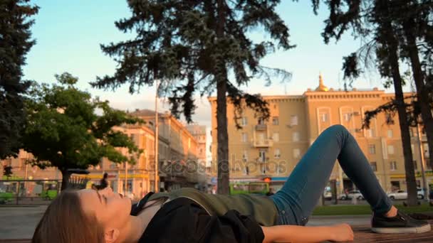 Блондинка лежит на скамейке и поднимает руку к небу — стоковое видео