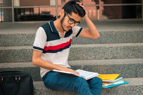 Siyah saçlı genç adam merdivenlerde oturur ve kitap haline benziyor