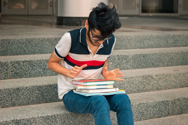 young student sits on the steps and looks at books