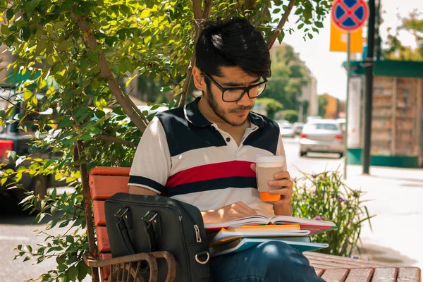 Knappe jongen in glazen die zit op de straat drinken koffie en het lezen van een boek — Stockfoto