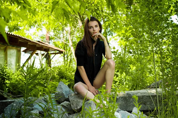 Schlanke schöne Dame in einem schwarzen Kleid sitzt in der Natur — Stockfoto