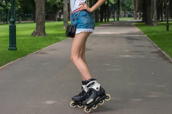 Slender legs of a young girl in denim shorts that rolls around in the park — Stock Photo, Image