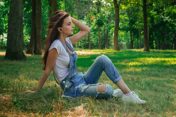 Young lovely girl sits on a grass and listening music — Stock Photo, Image