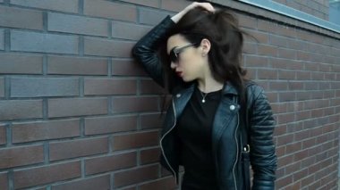 esmer siyah gözlük kırmızı ruj ve kameraya poz bir deri ceket bir duvara yakın: