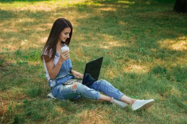 bir fincan kahve tutarak ve laptop arıyorum güzel kız çimenlerin üzerinde oturur