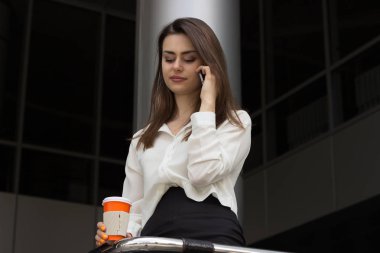 Cep telefonu ile konuşurken kahve olan esmer kadın