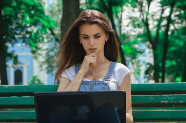 Bir bankta bir dizüstü bilgisayar kullanan ciddi genç esmer kız