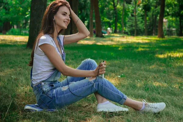 Charmante jolie fille assise sur l'herbe dans le parc et écoute de la musique — Photo