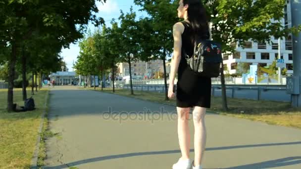 Bela menina esporte em um vestido preto e com uma mochila andando pela rua — Vídeo de Stock