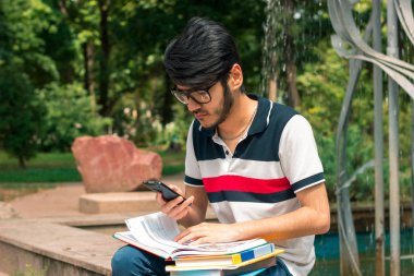 Genç esmer öğrenci çocuk kitaplarında bir cep telefonu kullanarak el ile