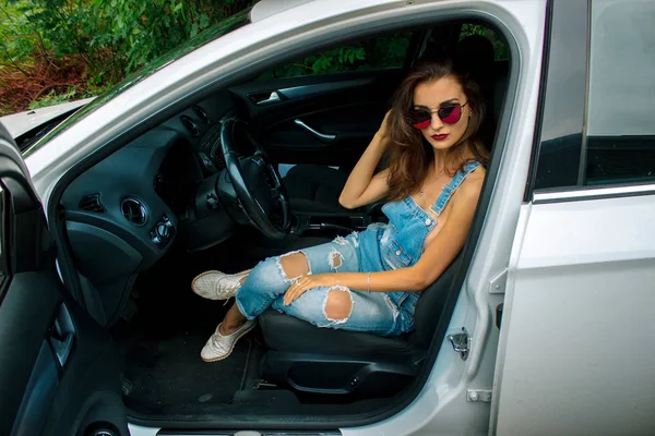 Mode belles femmes est assis dans la voiture et regarde dans la caméra — Photo