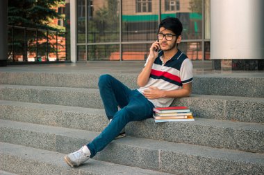 kitap ve telefon için geçiş ücretleri ile merdivenlerde oturan genç öğrenci