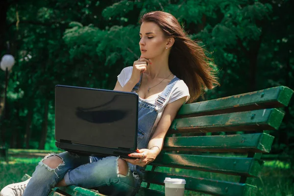 个年轻迷人的女孩坐在一个公园，一台笔记本电脑 — 图库照片