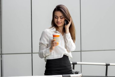 genç çekici iş bir fincan kahve ve telefonda konuşurken tutan kadın