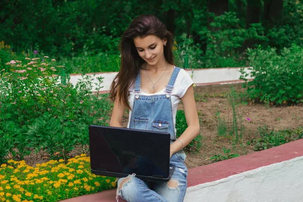 公園で座っている若い女の子の笑顔とノート パソコンで印刷 — ストック写真