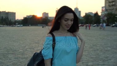 güzel gülümseyen esmer sokakta akşamları duruyor ve kameraya doğru görünüyor