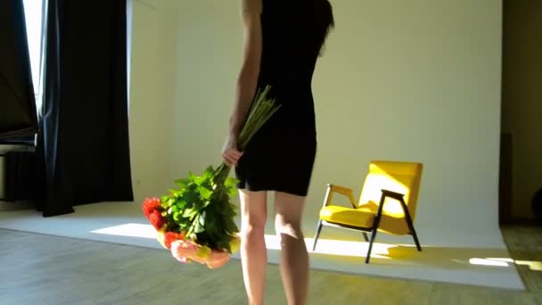 Mädchen im sexy schwarzen Kleid geht mit einem Blumenstrauß in der Hand ins Studio — Stockvideo