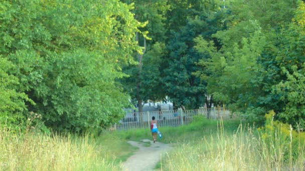Kvinna med en vatten väska och steg på gröna stigen i parken — Stockvideo